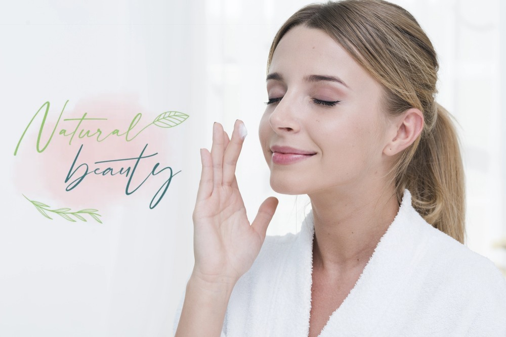 Elegant handwritten logo design for Natural Skin Beauty with soft green and teal tones on blush pink.